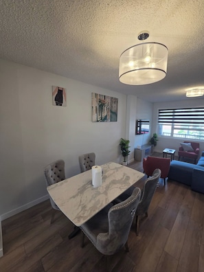 Un espace repas avec une table en marbre, des chaises rembourrées et un lustre.