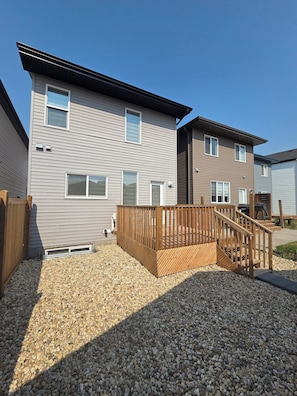 Un immeuble résidentiel à deux étages doté d’une terrasse en bois et d’une allée gravillonnée.