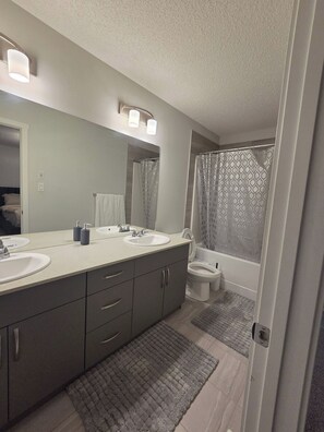 Une salle de bain moderne avec un meuble-lavabo à deux vasques, des toilettes et un espace douche.