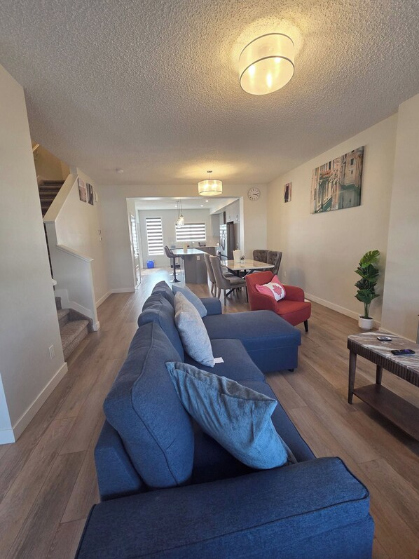 Un salon moderne comprenant un canapé d’angle, un coin repas et un escalier menant à un autre niveau.