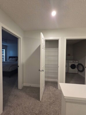 A room with a bed, a closet with shelves, and a laundry area with washing machines. - Spacious Family House in Edmonton - Perfect for a Comfortable Stay (Edmonton)