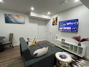 A modern living room with a grey sofa, a small round table, and a mounted TV displaying a live news channel. - Cozy Retreat With Private Entrance in Edmonton (Edmonton)