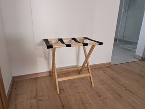 A wooden drying rack with black straps against a white wall, wooden flooring, and a glass door in the background.