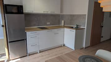 Eine kompakte Küche mit weißen Schränken, einem Edelstahlkühlschrank, einer Holz Arbeitsplatte und einem Spülbecken.