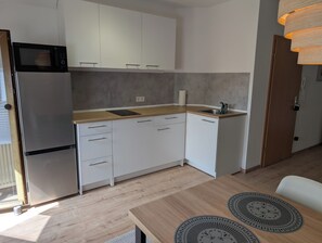 A compact kitchen with white cabinets, a stainless steel refrigerator, a wooden countertop, and a sink.