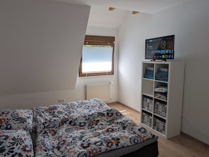 Un dormitorio con cama, ventana, radiador y televisor en un estante.