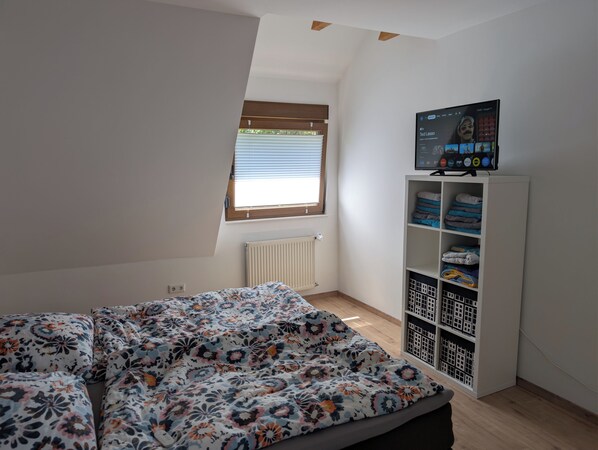 A bedroom with a bed, a window, a radiator, and a TV on a shelf.