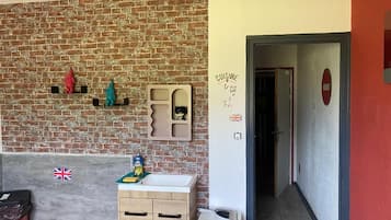 Een kamer met een bakstenen muur, een kleine keukenhoek en een deur naar een andere kamer.