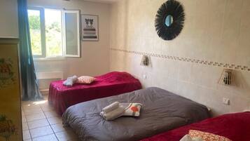 Habitación de hotel con dos camas, una ventana con cortinas, un espejo montado en la pared y un muro con azulejos.