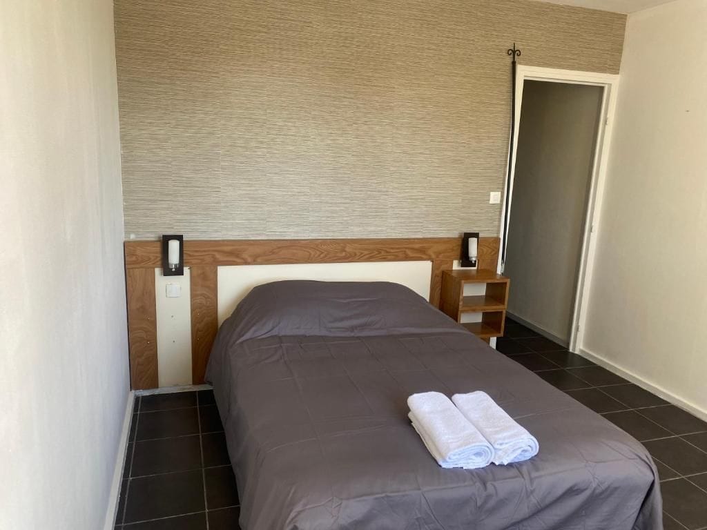 A hotel room with a bed, a nightstand, a wall-mounted lamp, and a door.