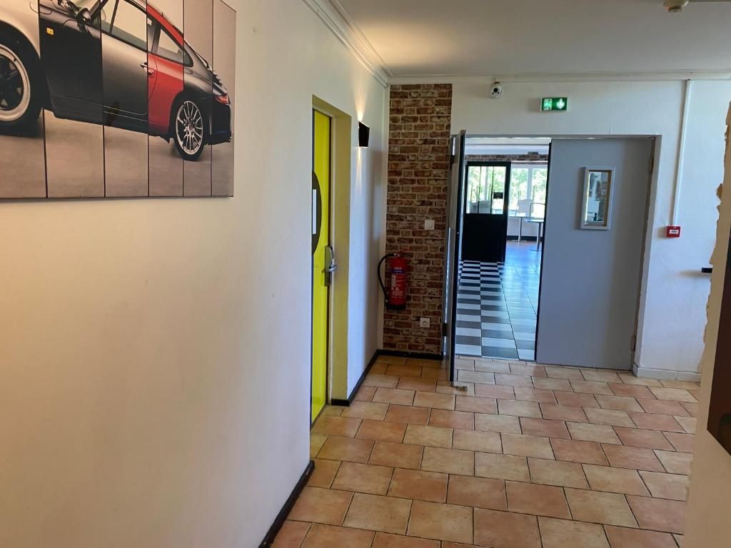 Een gang met een brandblusser, een deur met een gele hendel en een bakstenen muur.