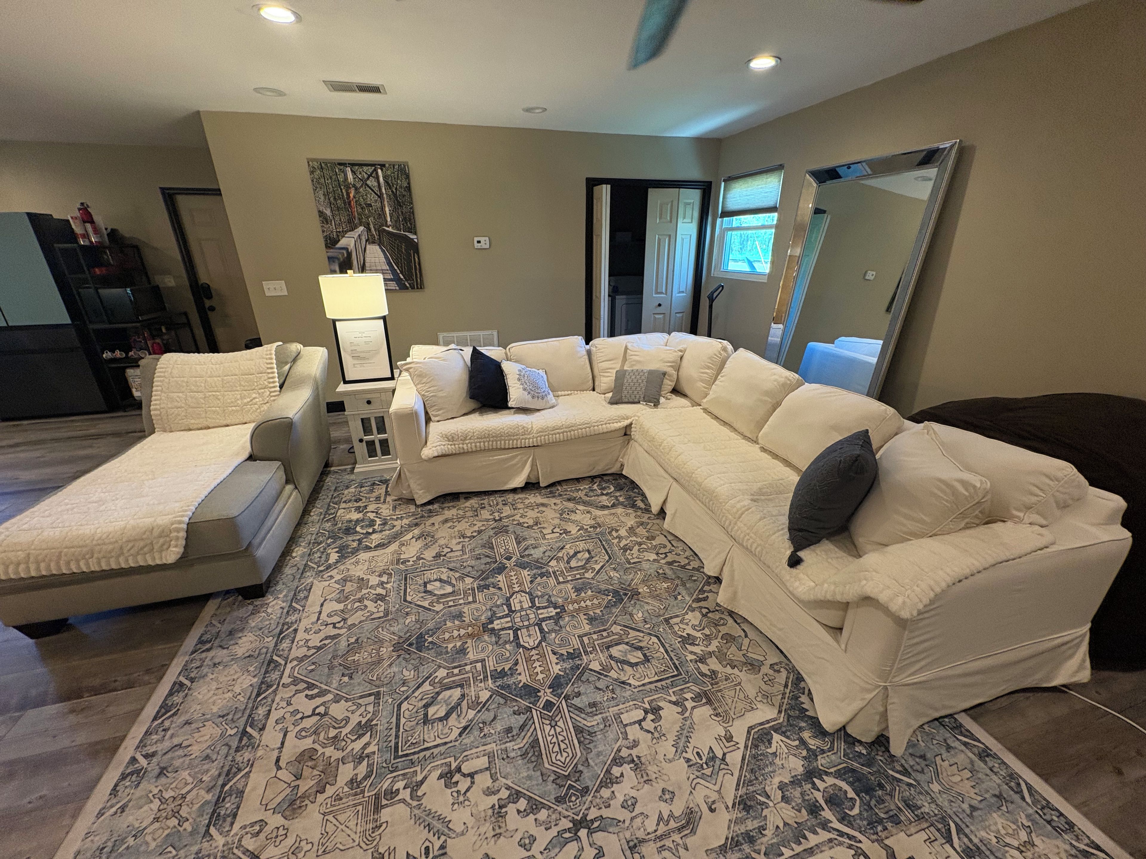 A living room with a sectional sofa, a chaise lounge, a patterned rug, and a large mirror.