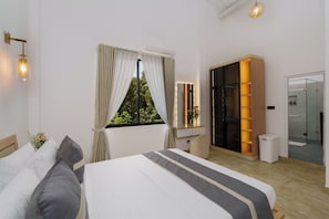 A modern hotel room with a large bed, a vanity with a mirror, a walk-in closet, and a glass shower.
