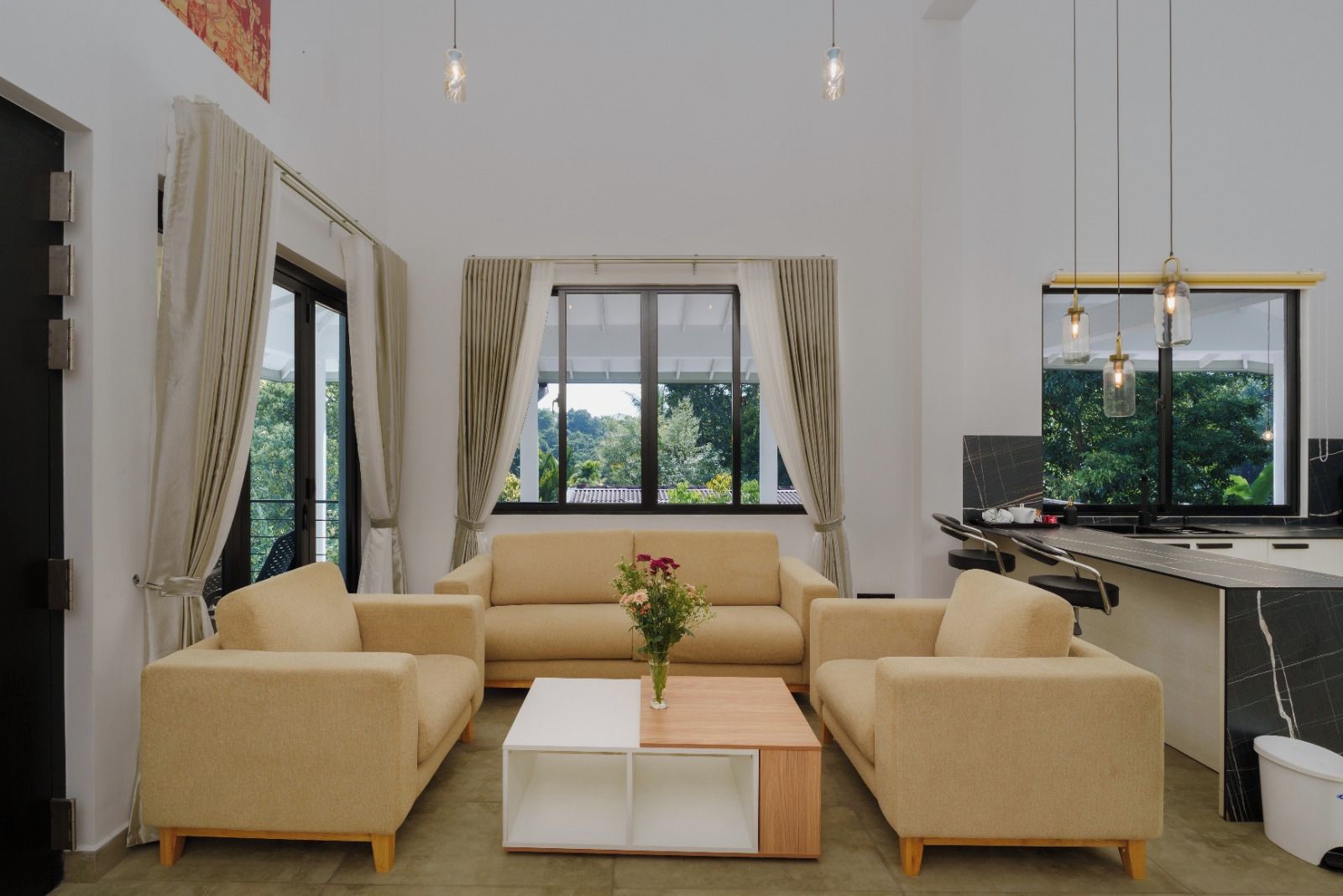 Ein modernes Wohnzimmer mit einem beigefarbenen Ecksofa, einem weißen Couchtisch und Blick auf Grünpflanzen durch große Fenster.