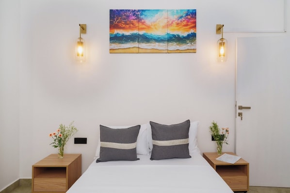 Une chambre à coucher avec un lit, deux tables de chevet, une commode, un tableau et des lampes fixées au mur.