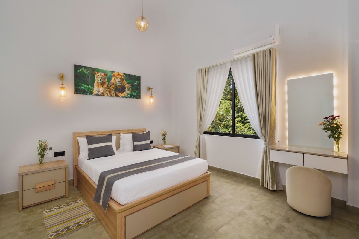 Quarto de hotel com cama, mesas de cabeceira, escrivaninha com espelho, janela com cortinas e pintura de leões.