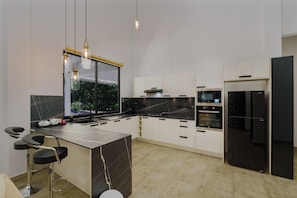 Une cuisine moderne dotée d’un îlot en marbre, d’appareils électroménagers noirs et de luminaires suspendus.