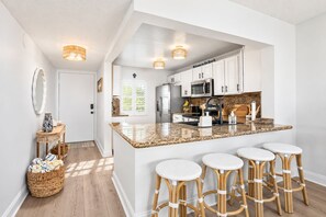 A modern kitchen with a central island, bar stools, and a view into the dining area. - Dunes Dream Just 100 Steps from the Beach (Jensen Beach)