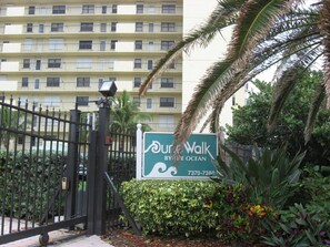A gated entrance with a sign for 'Dune Walk By The Ocean' and a multi-story building in the background. - Dunes Dream Just 100 Steps from the Beach (Jensen Beach)