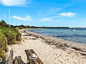 A sandy beach with a wooden bench and a hat placed on it, overlooking calm waters and a clear sky. - 4 Person Holiday Home in Ronde (Ronde)