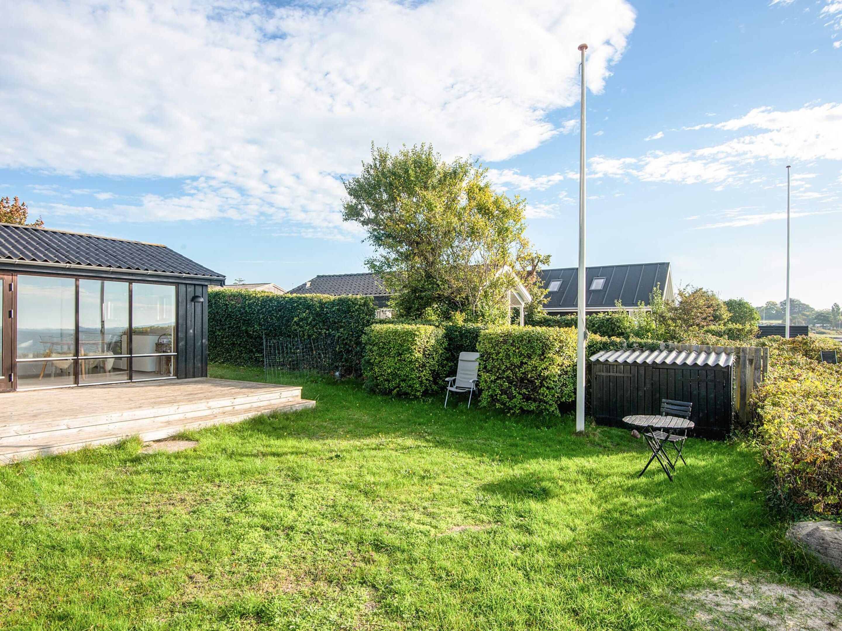 En moderne udendørs terrasse med glasafskærmning, træterrasse og velplejet græsplæne.