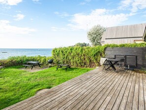 A wooden deck with picnic tables and a grill, overlooking a body of water. - 4 Person Holiday Home in Ronde (Ronde)