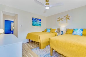 Habitación de hotel con dos camas, un ventilador de techo, un cuadro y una decoración de palmera.