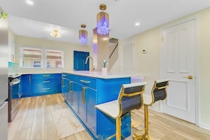 Una cocina moderna con armarios azules, encimera blanca y detalles dorados.