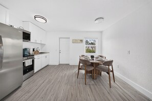 Cuina moderna amb electrodomèstics d'acer inoxidable, zona de menjador amb taula i cadires de fusta i vista per una finestra.