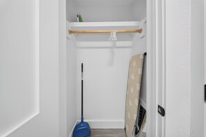 Passadís estret amb un esfregó recolzat a la paret, una taula de surf encostada a la pared, i una prestatgeria amb una ampolla verda.