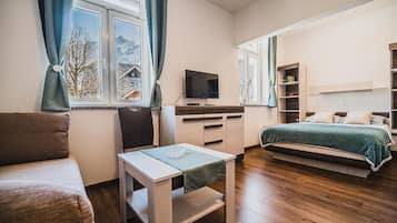 Un dormitorio con cama, televisión, escritorio y ventana con cortinas.