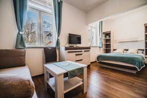 A bedroom with a bed, a TV, a desk, and a window with curtains.