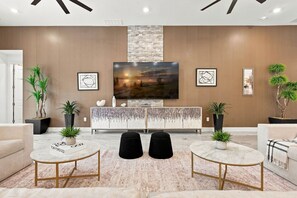 A modern living room with a large flat-screen TV, a stone fireplace, and a minimalist console table. - Luxury 15BR Suites, Pool and Themed Bedrooms (Williamsburg)
