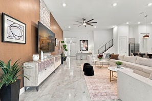 A modern living room with a marble floor, a sofa, a coffee table, and a TV mounted on the wall. - Luxury 15BR Suites, Pool and Themed Bedrooms (Williamsburg)