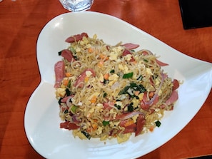 A white plate with a stir-fried dish containing vegetables and meat, placed on a wooden table. - Mapleview Hotel and Suites (Lekki)