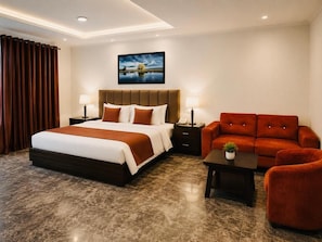 A hotel room with a large bed, a sofa, a small table, and a painting on the wall.