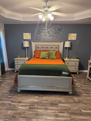 Ein Schlafzimmer mit einem Bett, zwei Nachttischen, einem Deckenventilator und dekorativen Wandbildern.