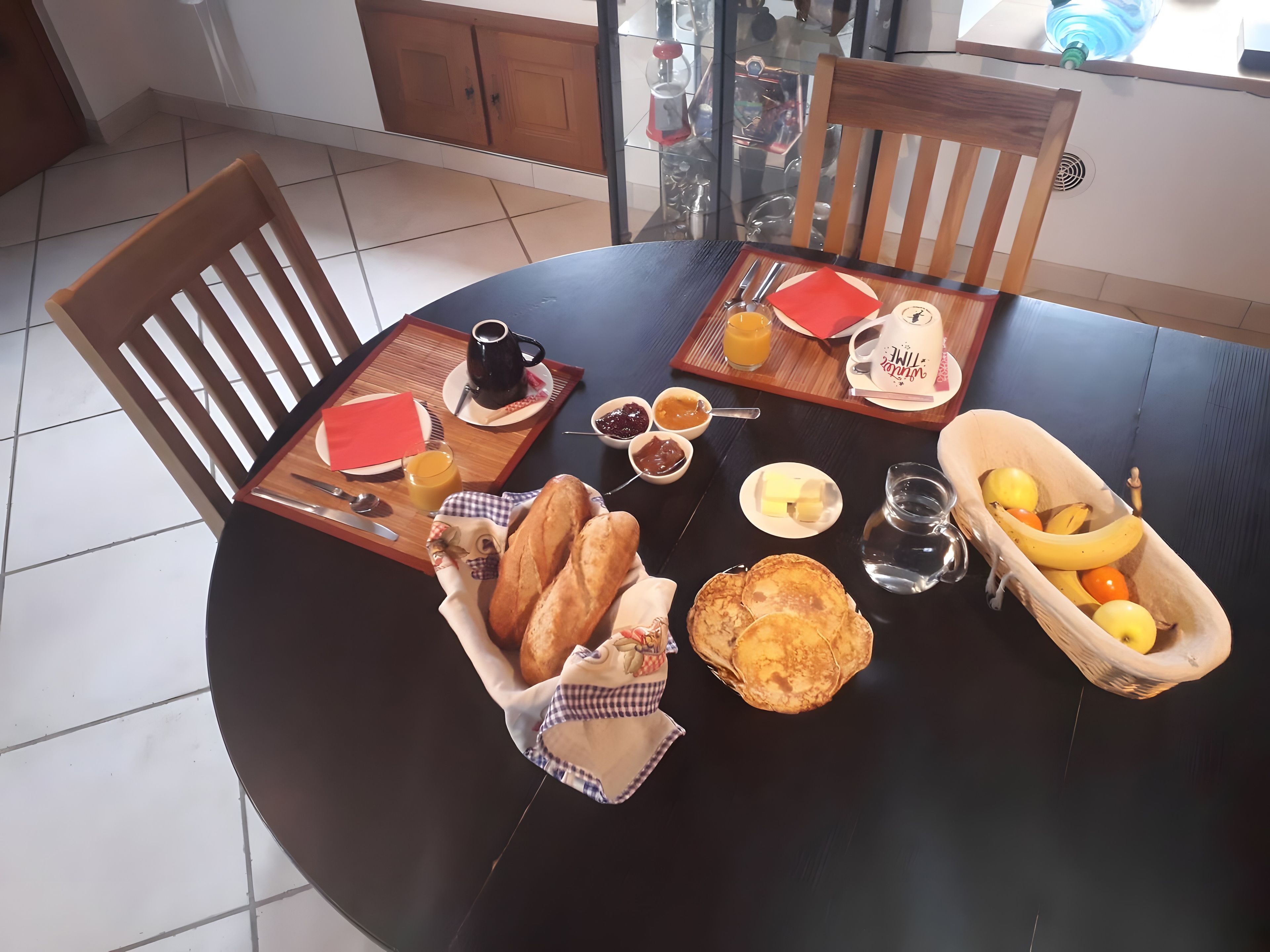 A round dining table set with breakfast items including bread, pancakes, fruit, and condiments.