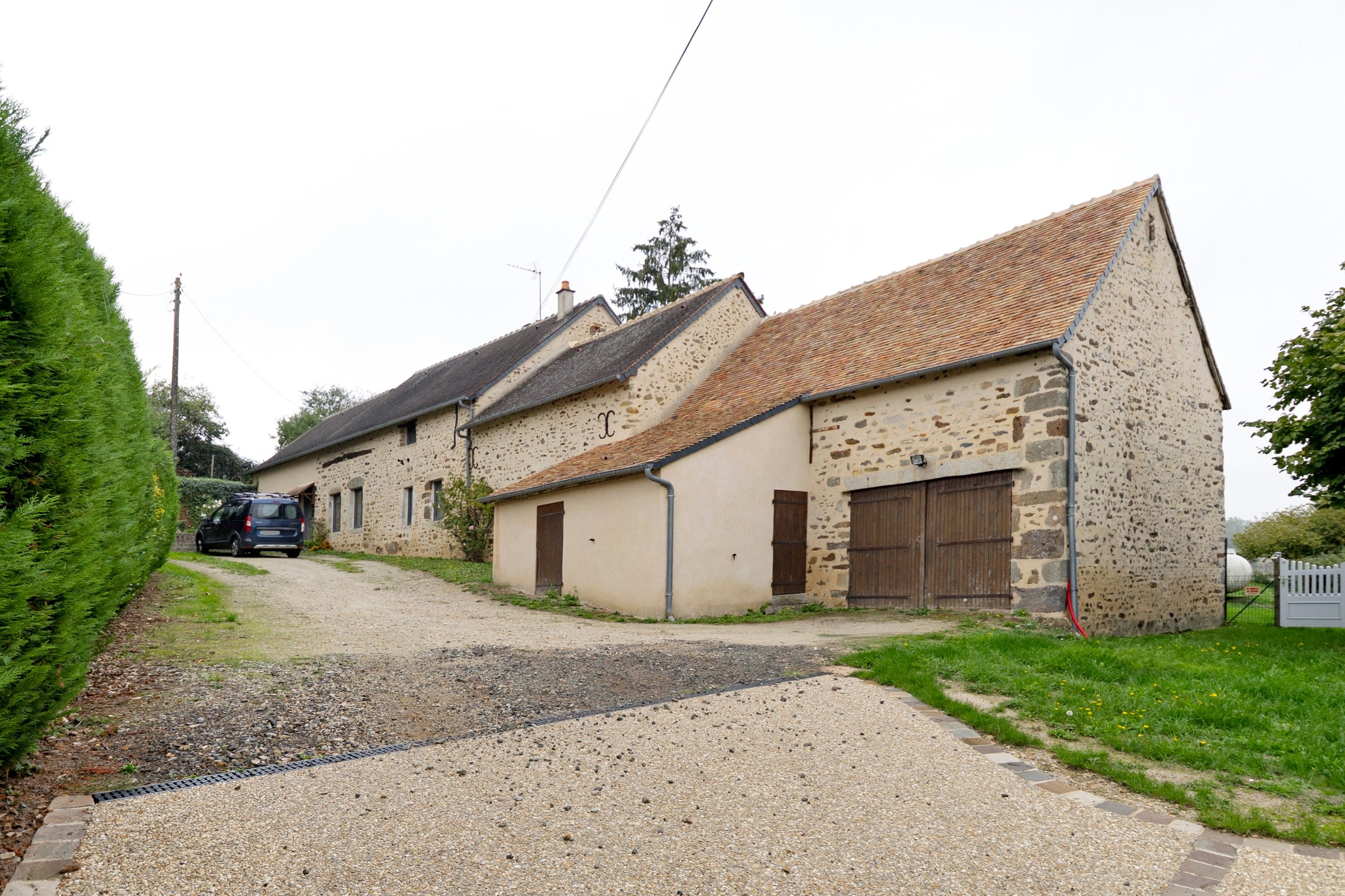 A rural property with a gravel driveway leading to a stone building with a tiled roof.