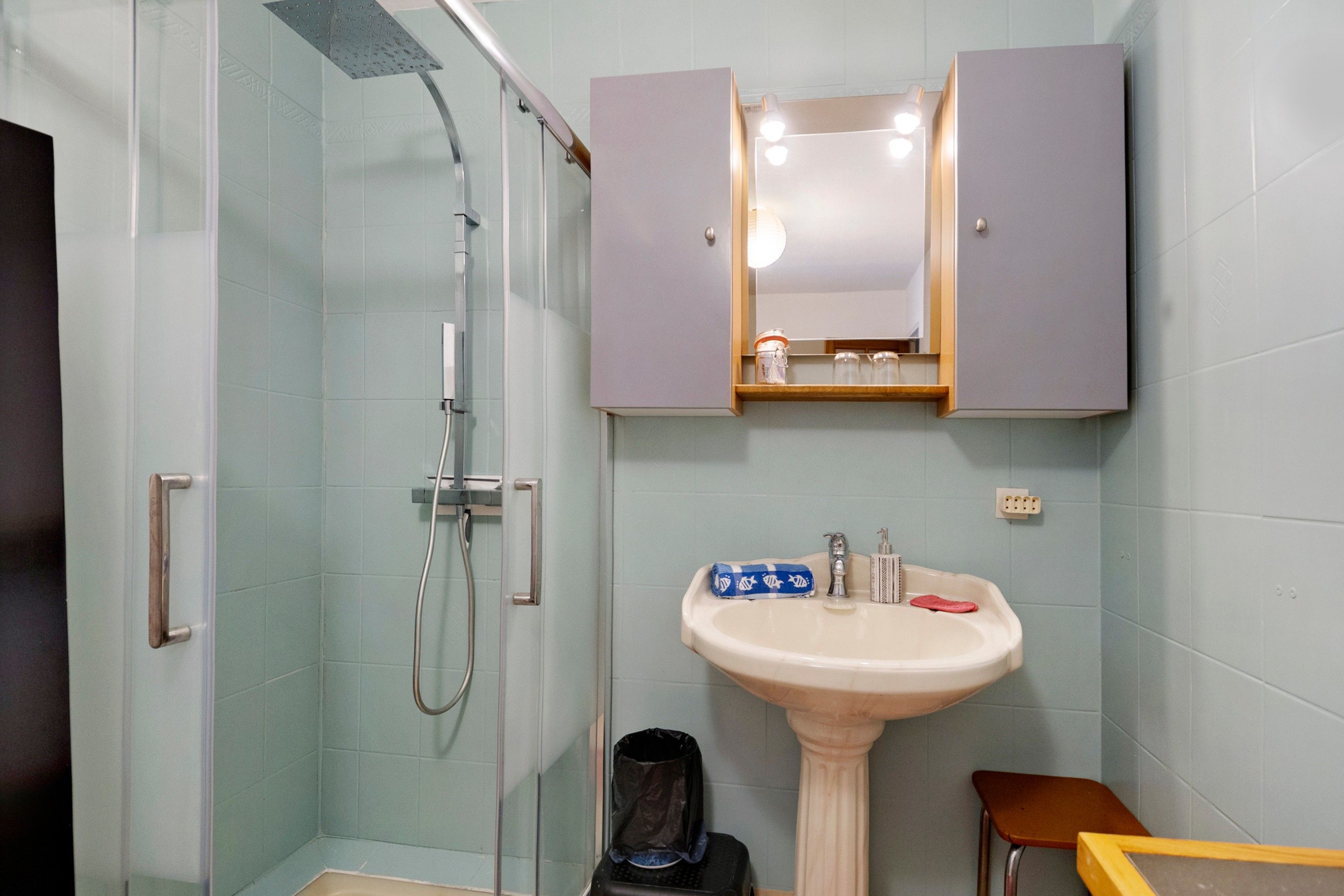 Een badkamer met douche, wastafel en kast.