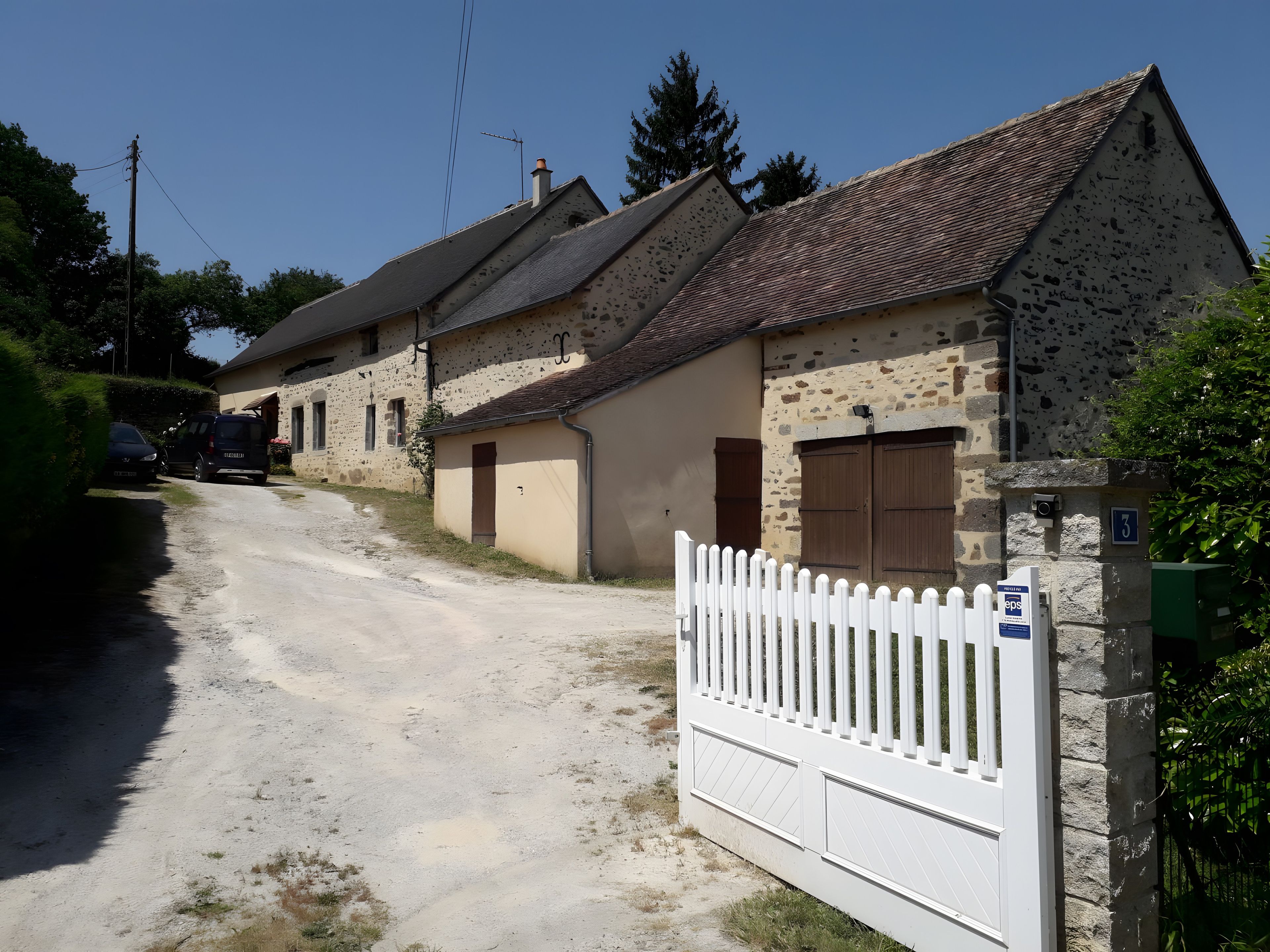 A rural road leading to a row of stone houses with a white picket fence.