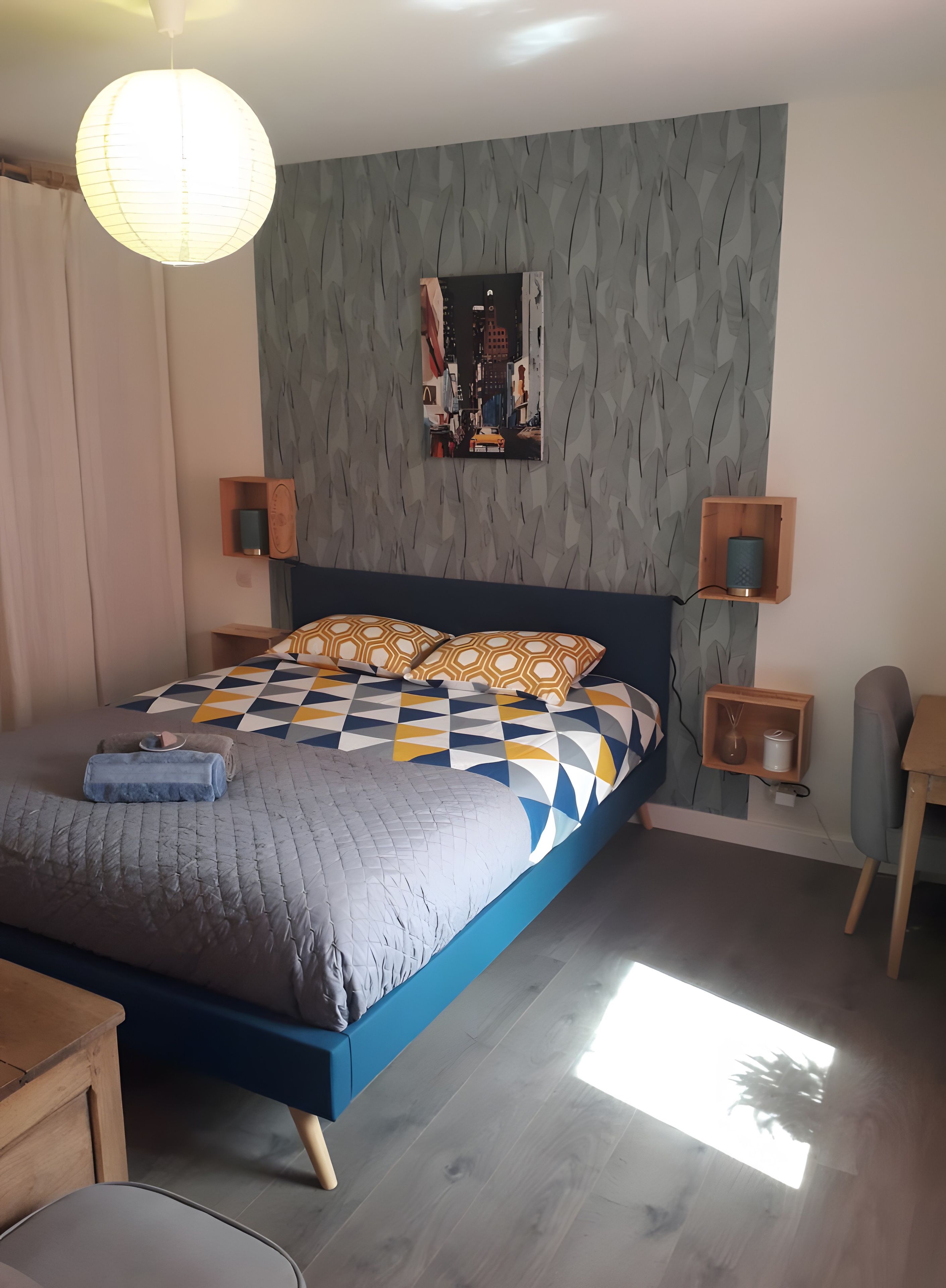 Ein Schlafzimmer mit einem Bett, einem Wandbild, Nachttischen und einer Pendelleuchte.