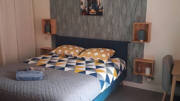 Ein Schlafzimmer mit einem Bett, einem Wandbild, Nachttischen und einer Pendelleuchte.