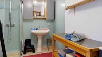 A bathroom with a shower, sink, mirror, and a wooden shelf with towels.
