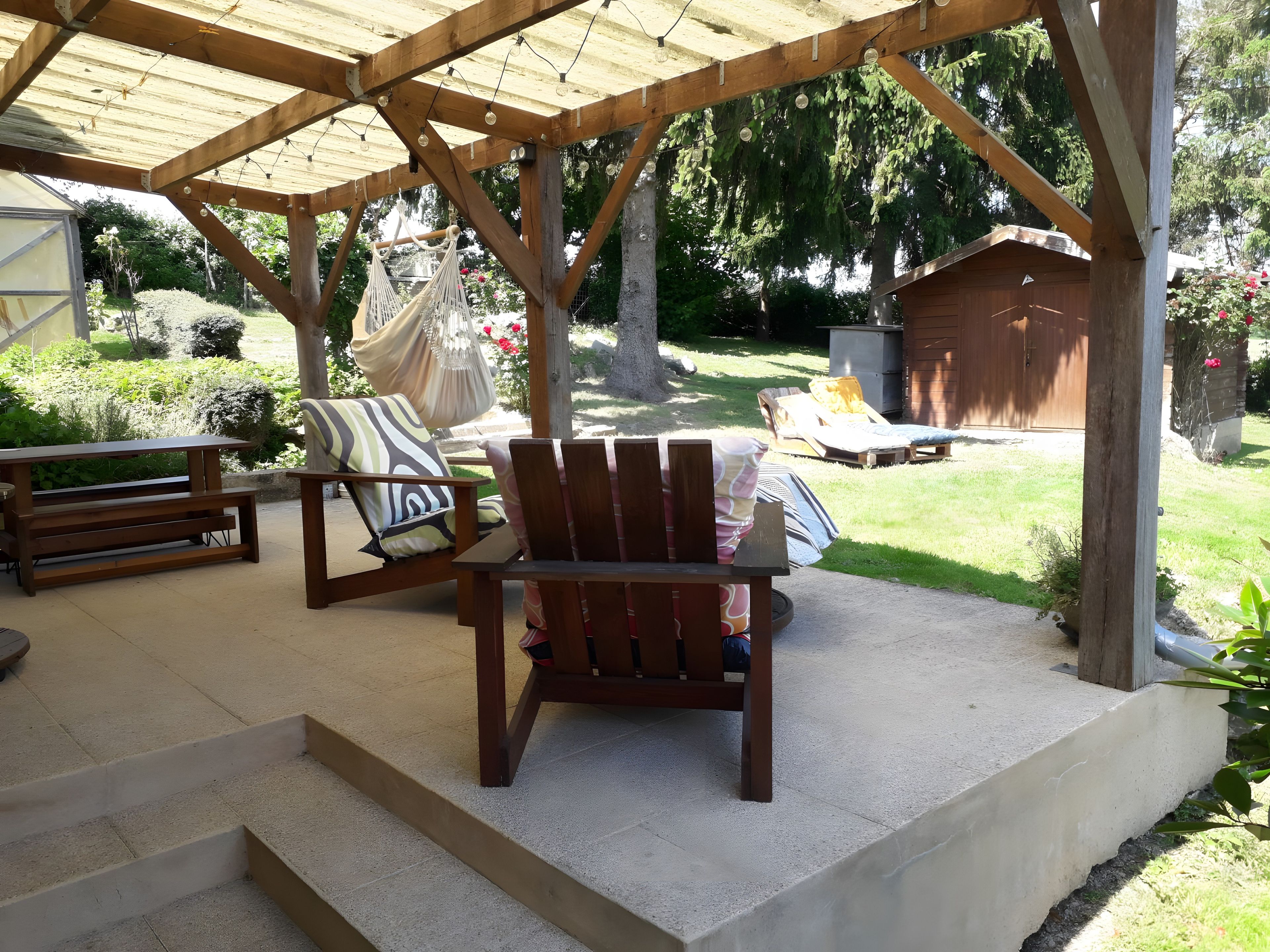 Een overdekt terras met een houten bank, een hangmat en een loungestoel.