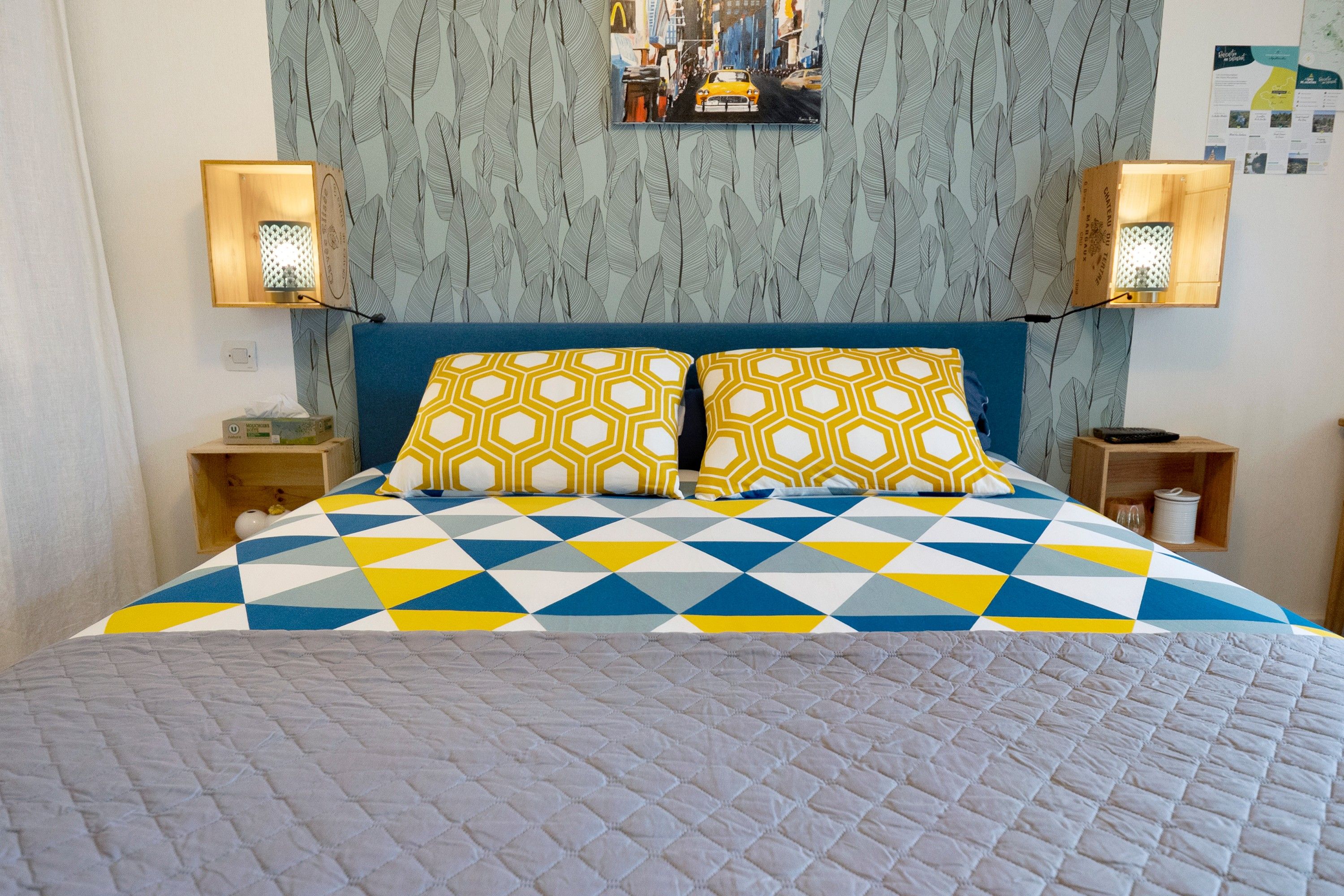 Un lit avec une couvre-lit à motifs géométriques, deux oreillers assortis et une tête de lit ornée d’un motif de feuilles.