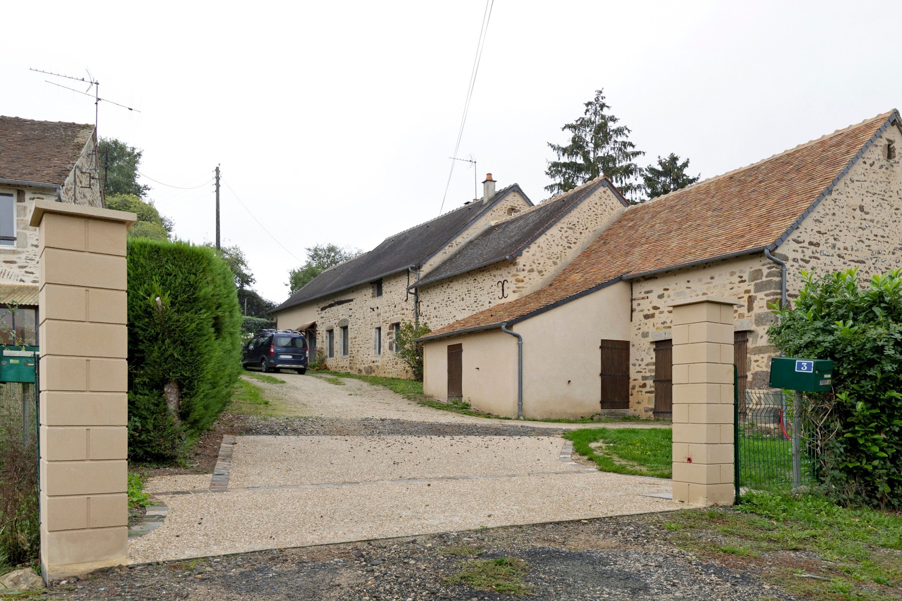 Une rue résidentielle bordée de maisons, avec une allée en gravier et une boîte aux lettres portant le numéro 3.