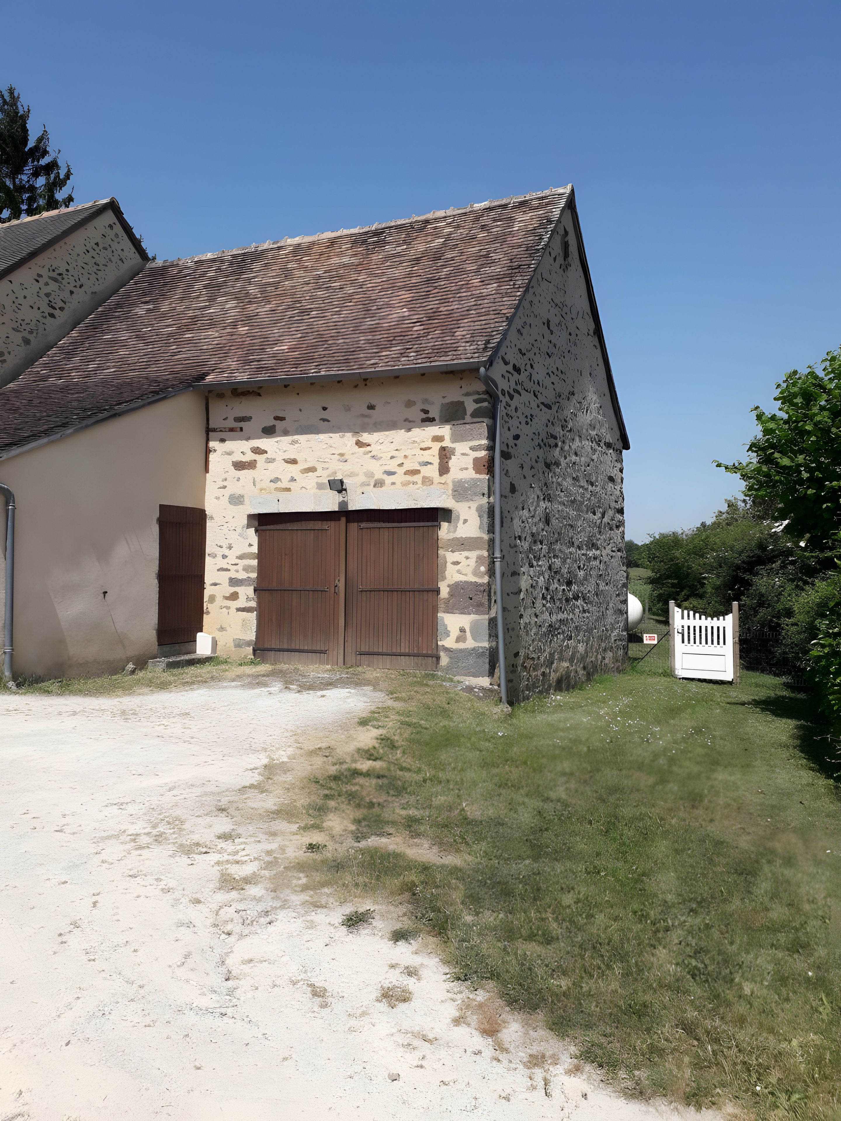 Un bâtiment en pierre avec un toit en tuiles, une porte en bois et une clôture blanche.