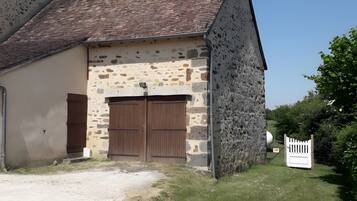 Un bâtiment en pierre avec un toit en tuiles, une porte en bois et une clôture blanche.