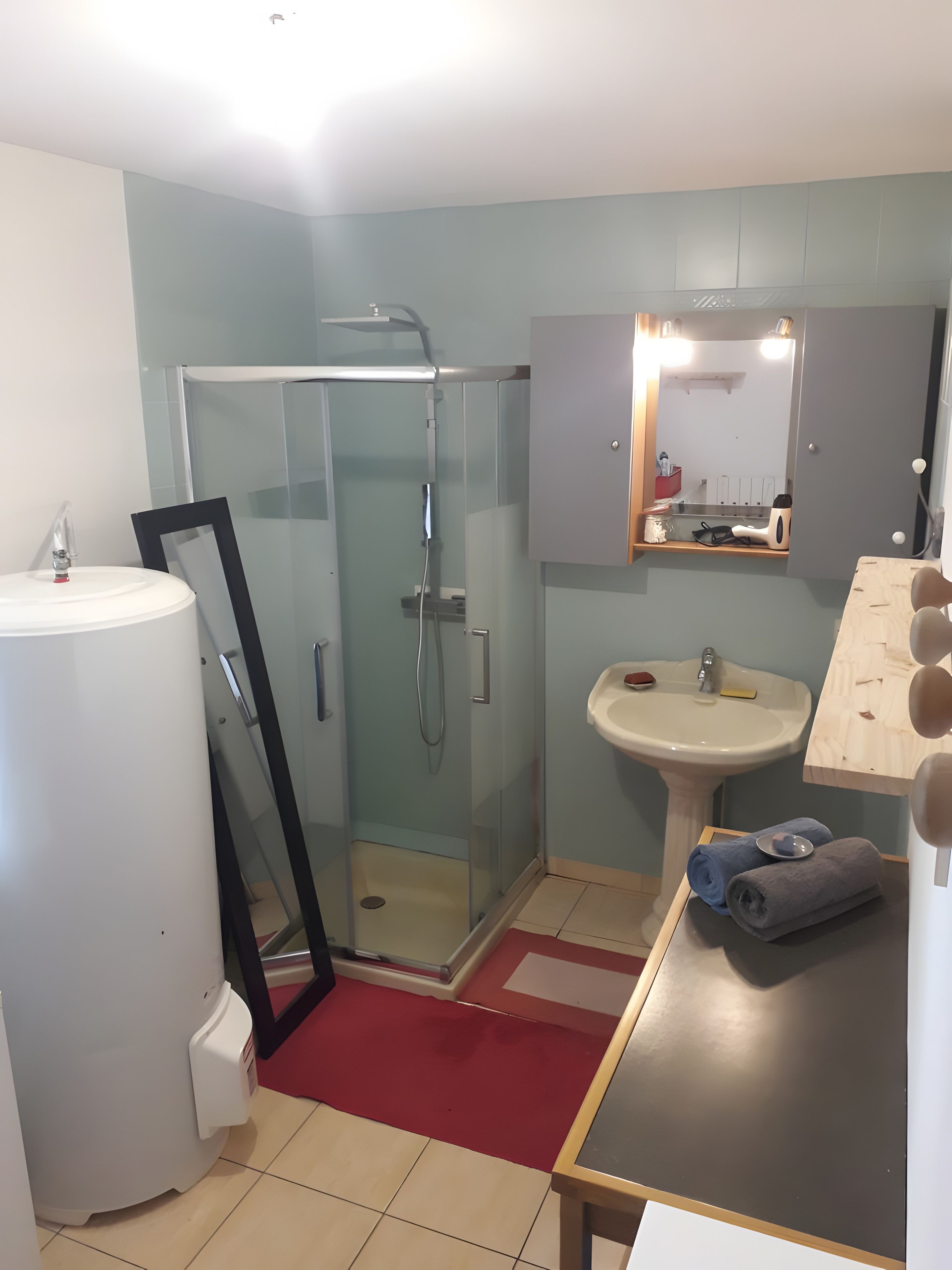 Une salle de bain avec une douche à parois de verre, un lavabo avec un miroir au-dessus et une serviette posée sur une table.